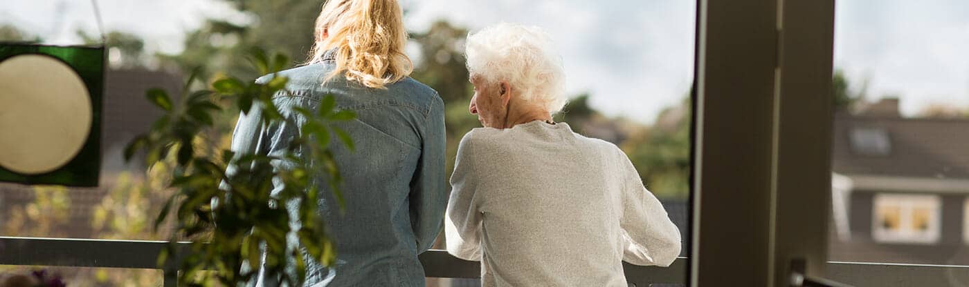 Frau steht mit älterer Frau auf Balkon
