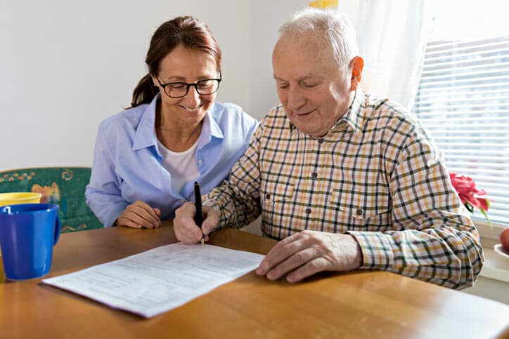 Pflegerin sitzt mit altem Mann an Formularen