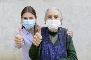 Pflegerin und ältere Frau mit Maske und Daumen hoch