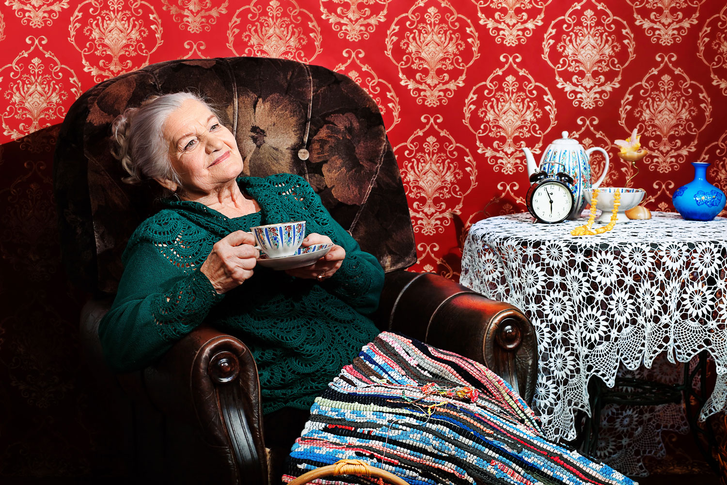 Ältere Dame sitzt lächelnd mit Tee im Sessel