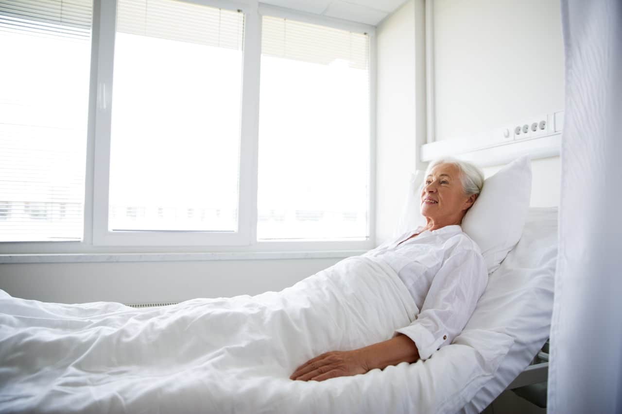 smiling senior woman lying on bed at hospital ward